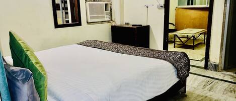A hotel room with a bed, a TV, an air conditioning unit, a desk, and a chair.