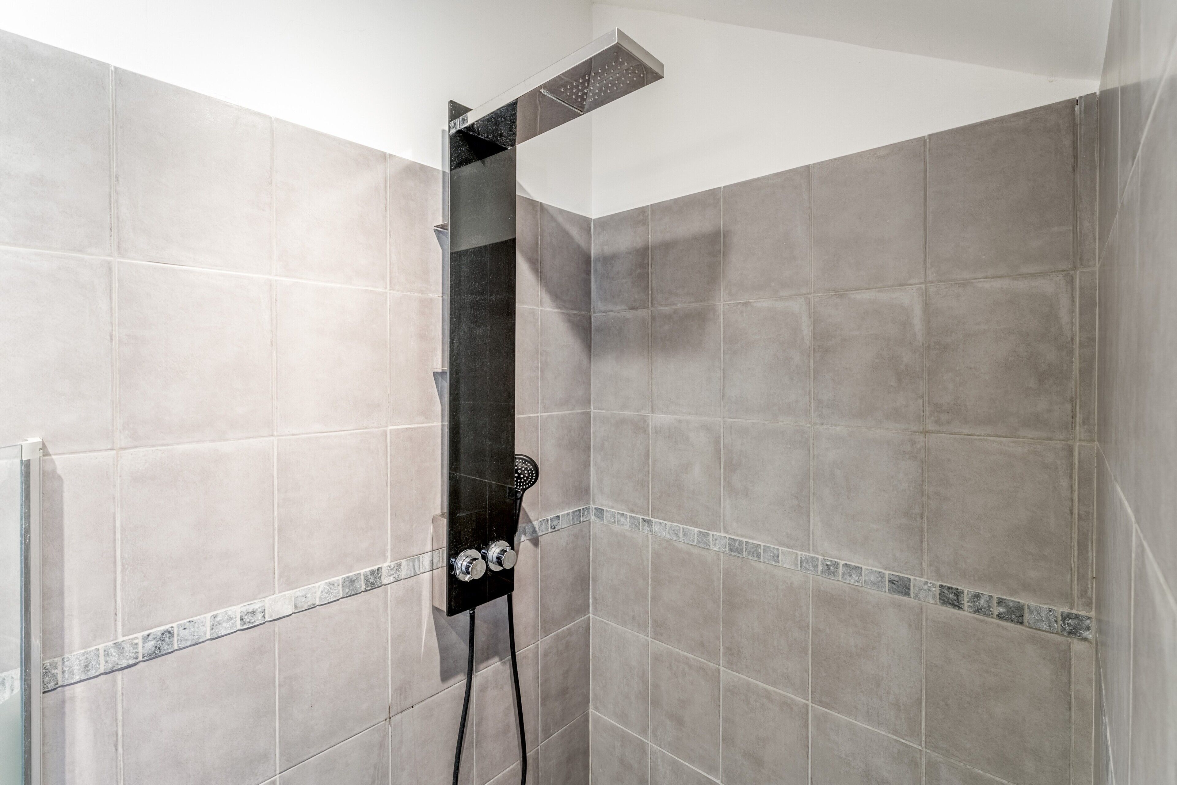 Une douche équipée d’un pommeau de douche à main et d’un panneau de commande fixé au mur.