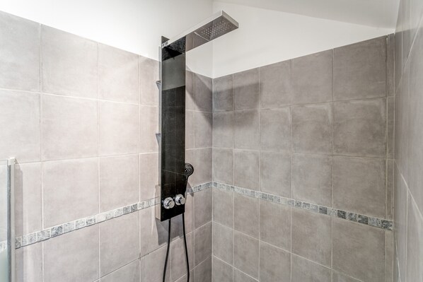 A shower with a handheld showerhead and a wall-mounted control panel.