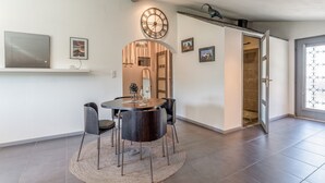 A dining area with a round table, chairs, a clock, and a door leading to a shower.