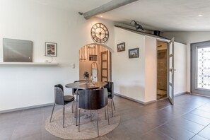 Ein Essbereich mit einem runden Tisch, Stühlen, einer Uhr und einer Tür zu einer Dusche.