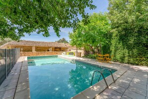 Ein Pool mit einem dahinterliegenden Steinhaus, umgeben von Bäumen.