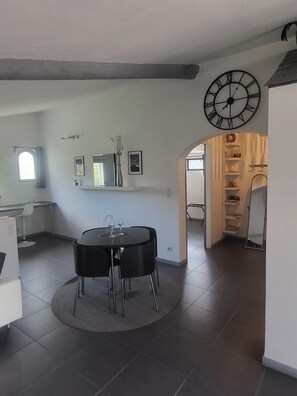 Un comedor con una mesa redonda y sillas, un reloj en la pared, y una ventana con cortinas.