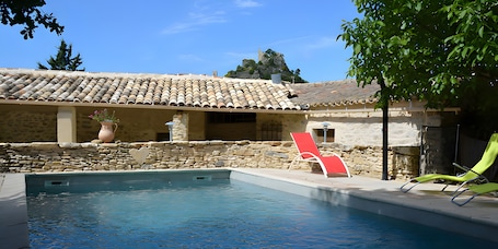 A swimming pool with a stone wall, a red lounge chair, and a stone building with a tiled roof.. Holiday Home 'Gîte De L'harmonie À Entrechaux' with Mountain View, Wi-Fi and Air Conditioning