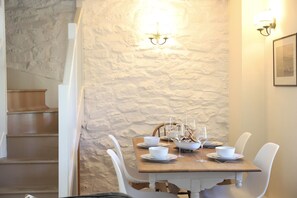 Un comedor con pared de piedra, mesa de madera, sillas blancas y una escalera.