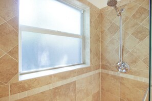 Brusebad med håndbruser, et vindue med satin glas og flisebeklædte vægge.