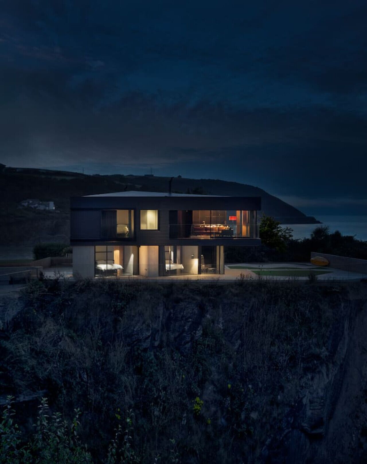 Une maison moderne à deux étages, dotée de grandes fenêtres, d’un balcon et offrant une vue sur la mer.
