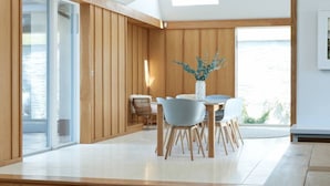 Un comedor moderno con interior de madera, un ventanal de vidrio que da al exterior y vistas al aire libre.
