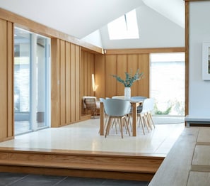 A modern dining area with a wooden interior, a glass door leading outside, and a view of the outdoors.