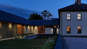 Una casa moderna con fachada iluminada, camino de grava y jardín con flores.