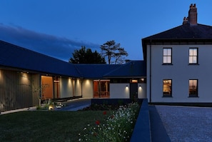 A modern house with a well-lit exterior, a gravel driveway, and a garden with flowers.