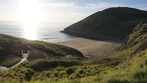 Un paisaje costero con un camino que lleva a una playa, rodeado de colinas cubiertas de hierba.