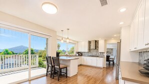 Uma cozinha moderna com uma ilha grande, armários brancos e vista para uma montanha.