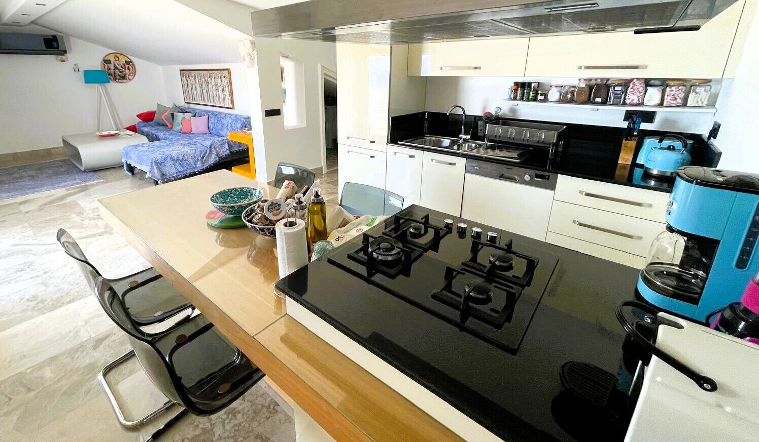 A modern kitchen with a gas stove, a coffee machine, and a dining area with a table and chairs.