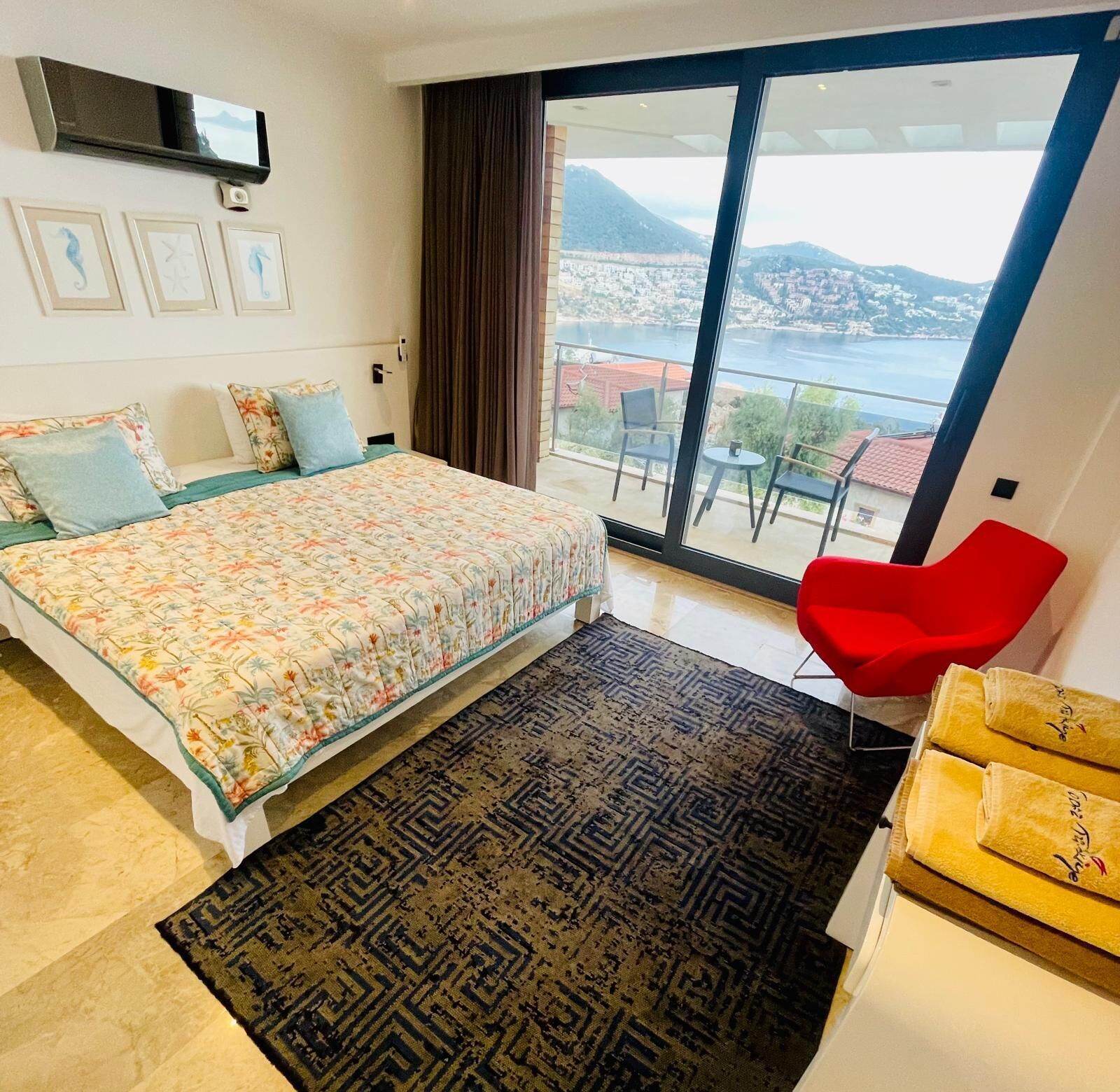 A bedroom with a bed, a red chair, a TV, and a balcony with a view.