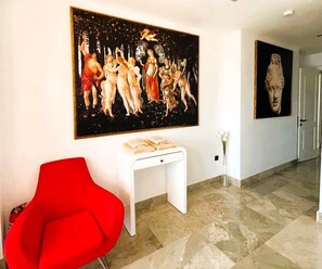 Ein Flur mit einem roten Sessel, einem weißen Beistelltisch und einem großen Gemälde an der Wand.