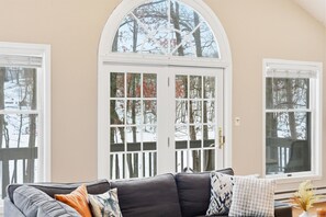 Ein Wohnzimmer mit einem dunkelgrauen Sofa, einem großen Bogenfenster und einer Tür mit weißem Rahmen.