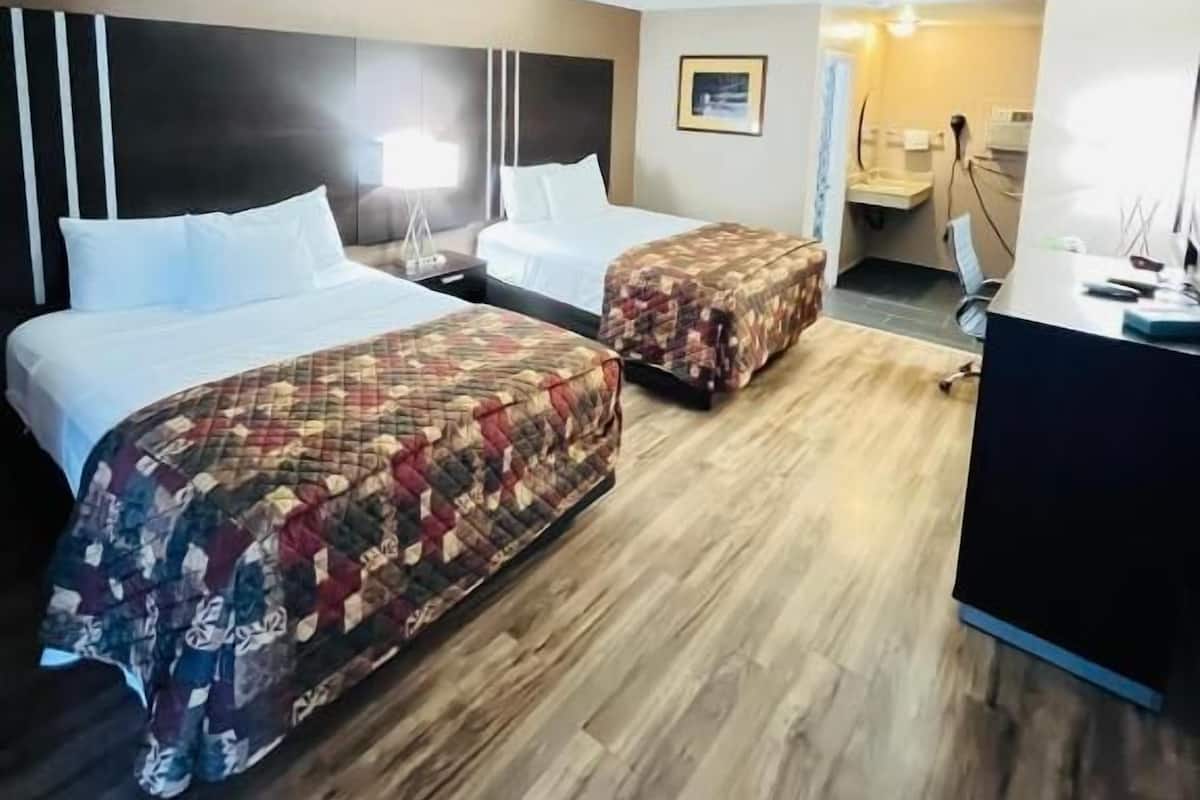 A hotel room with two beds, a desk, a chair, and a small kitchenette.