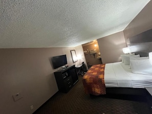 A hotel room with a bed, a desk, a television, and a wall-mounted air conditioning unit. - Star Inn (Tonopah)