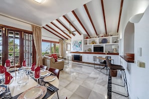 A dining area with a table set for four, a sofa, and a kitchen area with a TV and shelves. - W12 Andalusian style villa with sea views (Mijas Costa)