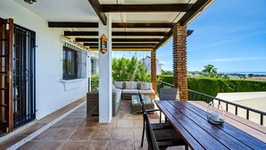 A covered patio with a wooden table and chairs, a sofa, and a view of the ocean. - W12 Andalusian style villa with sea views (Mijas Costa)