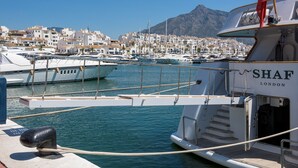 A marina with boats docked, a mountainous backdrop, and a building labeled 'SHAF LONDON' in the foreground. - W12 Andalusian style villa with sea views (Mijas Costa)