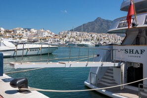 A marina with boats docked, a mountainous backdrop, and a building labeled 'SHAF LONDON' in the foreground. - W12 Andalusian style villa with sea views (Mijas Costa)