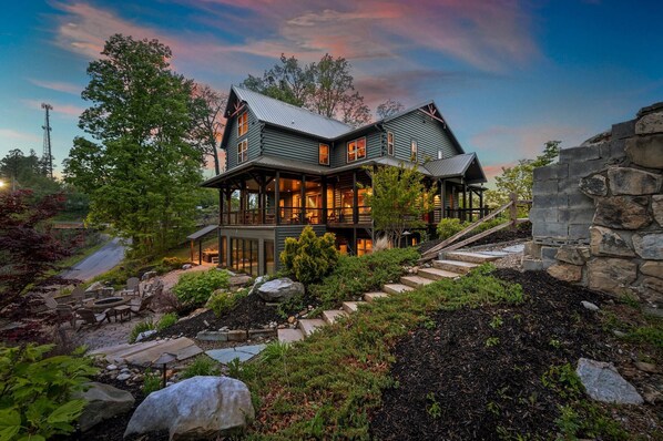Ein großzügiges, zweistöckiges Haus mit Natursteinfundament, einer Veranda und einem angelegten Garten mit Steinen und Pflanzen.