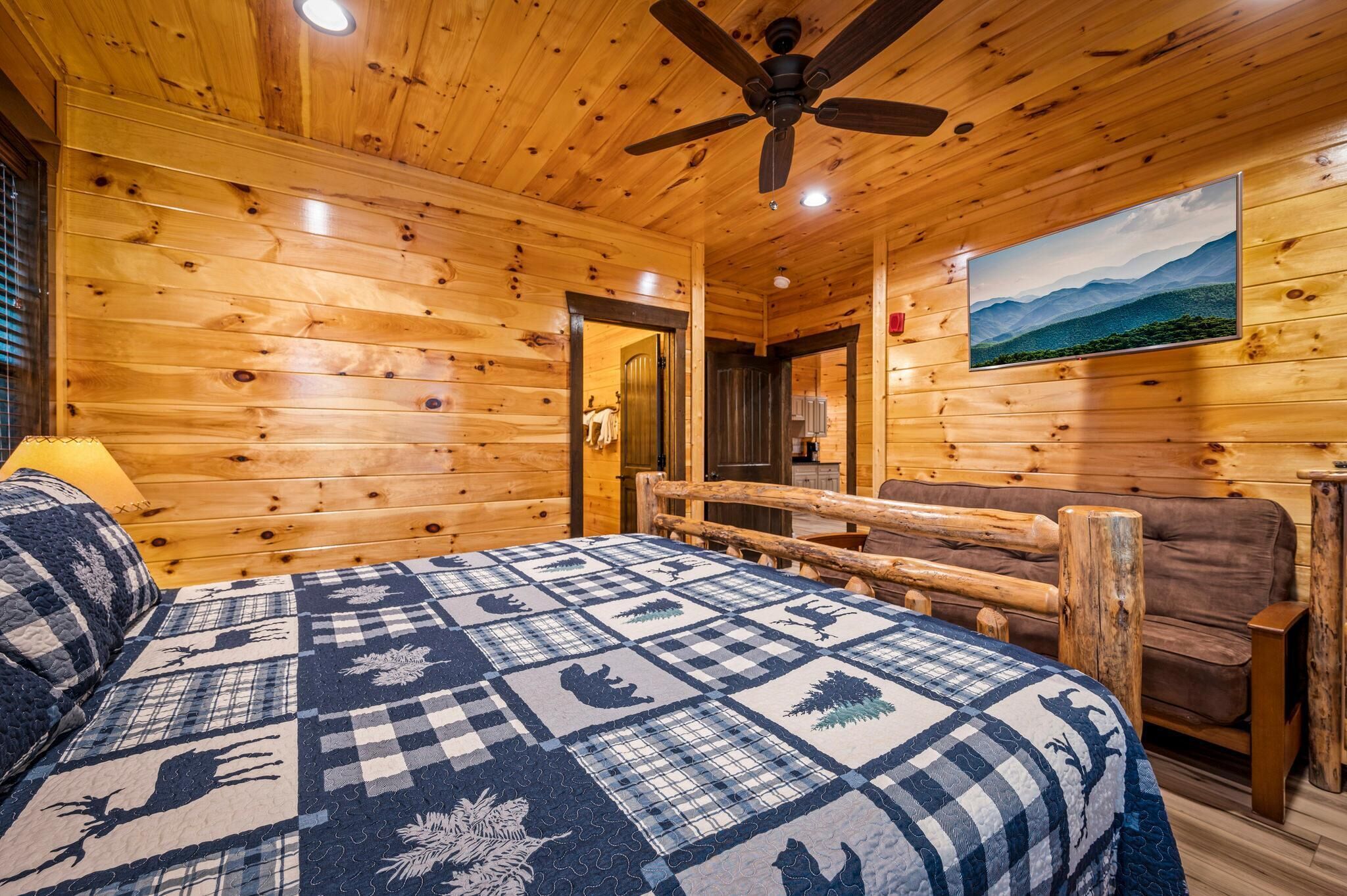 A wooden cabin room with a bed, a ceiling fan, a painting, and a wooden bench.