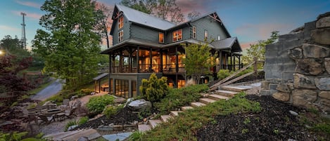 A large, two-story house with a stone foundation, a covered porch, and a landscaped garden with rocks and plants.