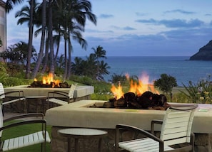 Un espacio de estar al aire libre con una chimenea, sillas y vista al océano.