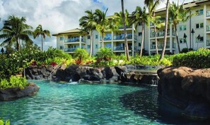Un resort con piscina cristalina, palmeras y un edificio de varios pisos con balcones.
