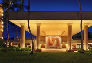 A hotel entrance with a large mural, palm trees, and classical columns.