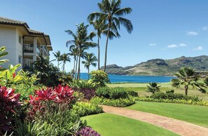 A hotel with a well-maintained lawn, palm trees, and a view of the ocean. - Christmas Holiday Luxury in Marriott's Kauaʻi Lagoons Oceanfront Resort! (Lihue)