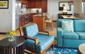 Una cocina moderna con electrodomésticos de acero inoxidable, una zona de comedor con sofá azul y cojines estampados, y una pequeña isla con fregadero.