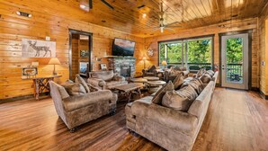 A log cabin interior with a fireplace, plush seating, and large windows. - The Great Maple Retreat (Gatlinburg)
