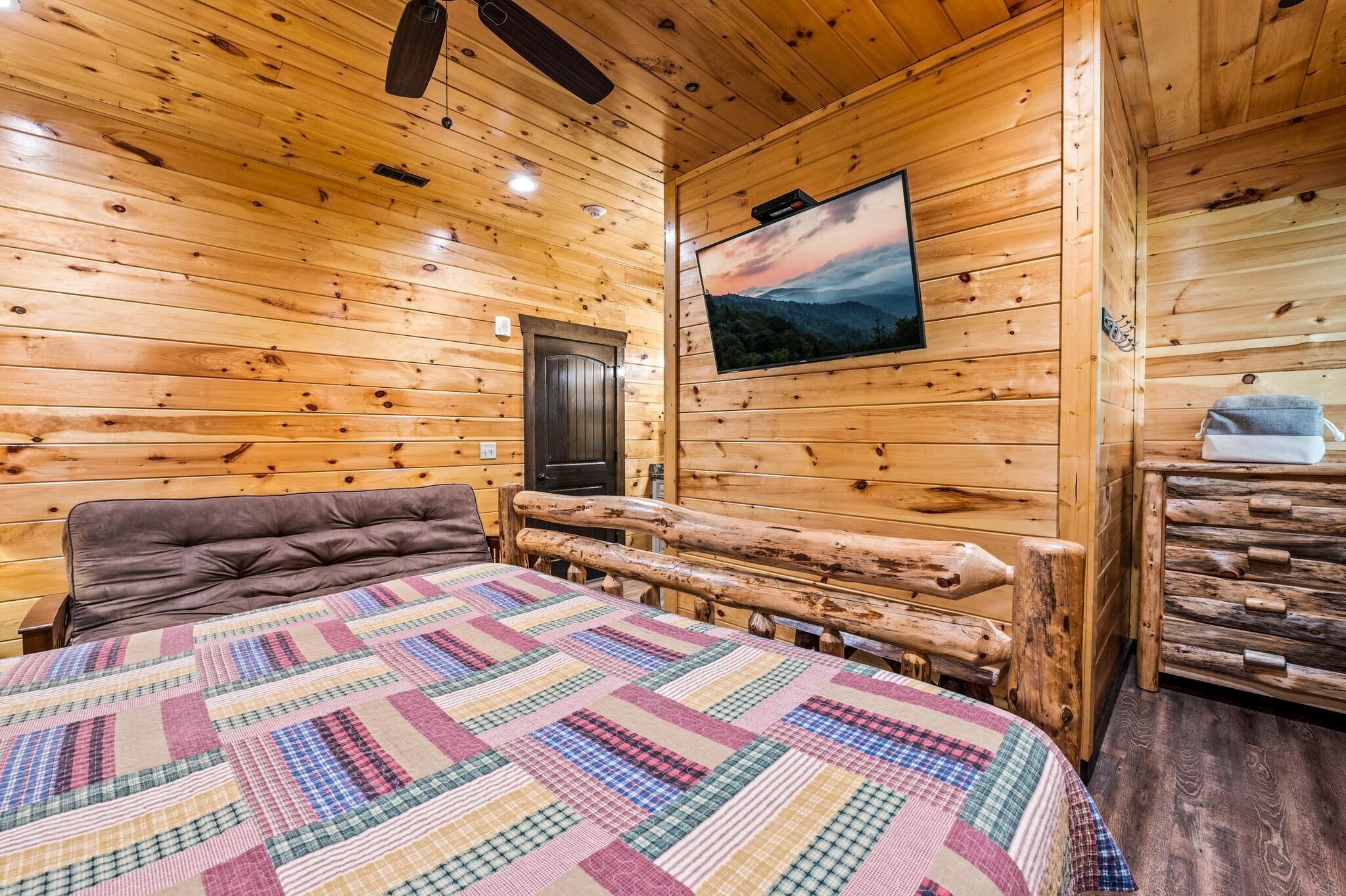 Una camera in una casetta di legno con un letto, una televisione e un comò in legno.