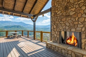 Eine Holzterrasse mit einem Steinkamin, Gartenmöbeln und einer schönen Aussicht auf die Berge.