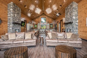 Ein geräumiges Holzblockhaus-Interieur mit Essbereich, zwei Ledersofas und einem Steinkamin.