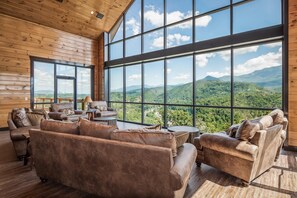 Ein geräumiger Raum mit Ledersofas, einem runden Couchtisch und großen Fenstern mit Blick auf die Berge.