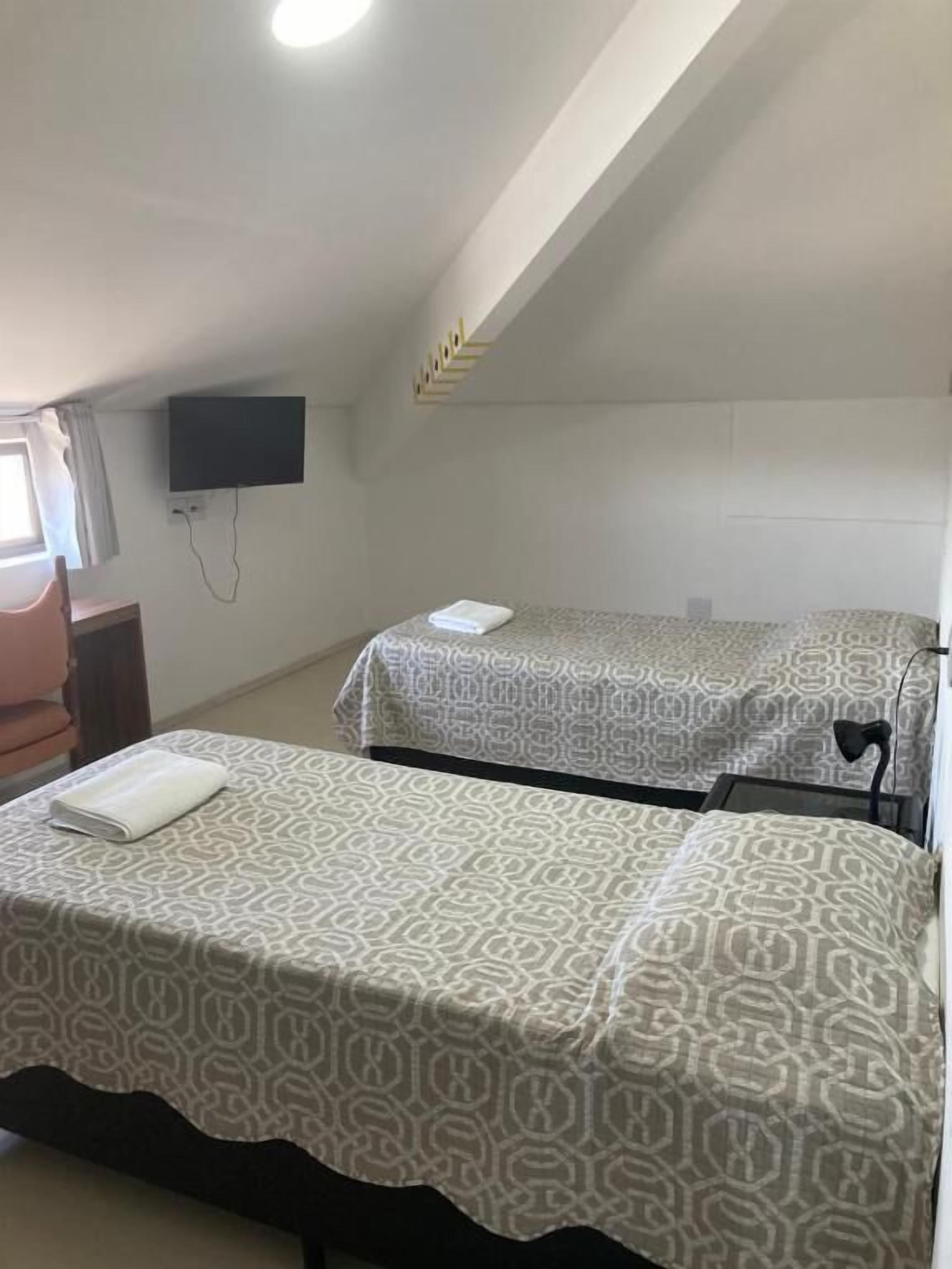 Une chambre avec deux lits, un téléviseur fixé au mur et une fenêtre avec des rideaux.