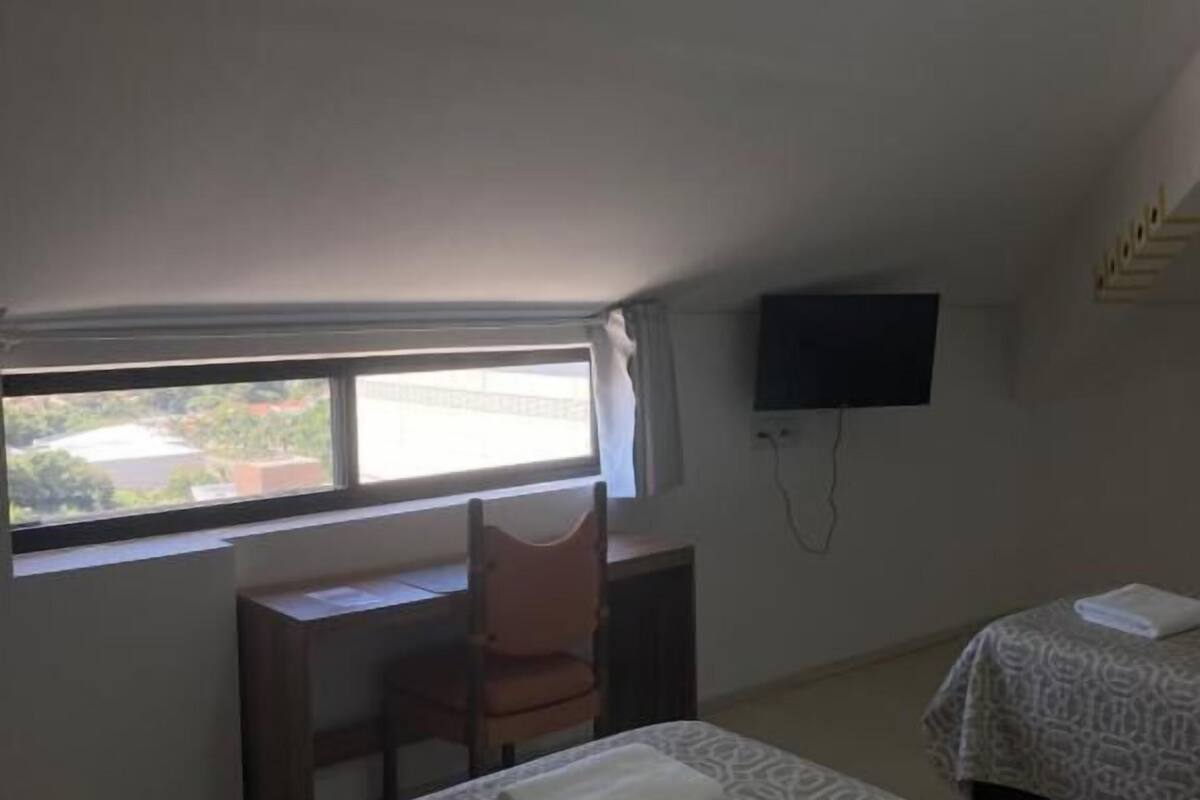 A room with two beds, a desk, a chair, a television, and a window with a view.