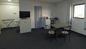 A room with a dining table, chairs, a TV, a microwave, and a window. - HAUSHostel (Vinhedo)