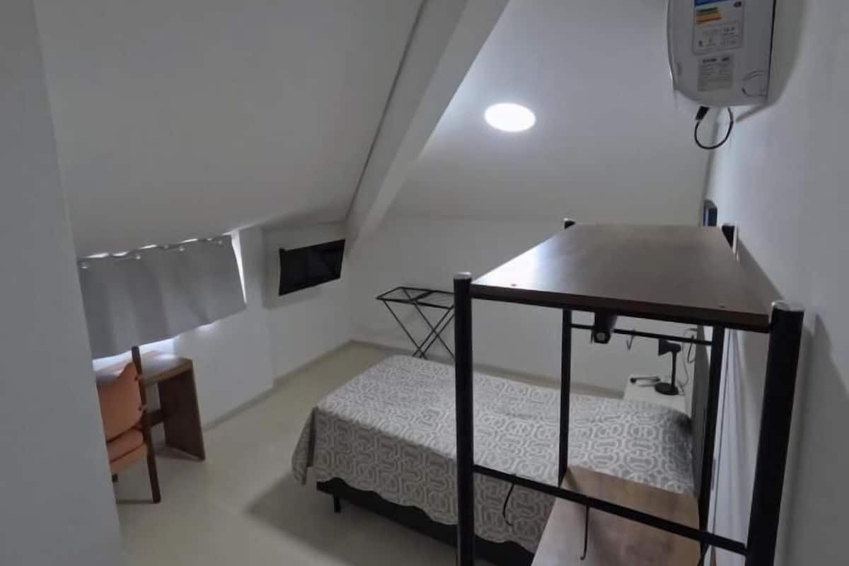 A small, triangular room with a bunk bed, a desk, and a chair.