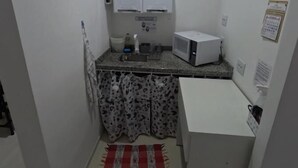 A small kitchenette with a microwave, a sink, and cabinets. - HAUSHostel (Vinhedo)
