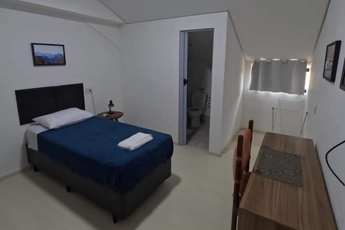 A bedroom with a bed, bedside table, and a desk with a chair.