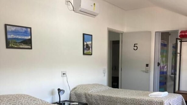 Two single beds with patterned bedding, a wall-mounted air conditioner, and a door with the number 5. - HAUSHostel (Vinhedo)