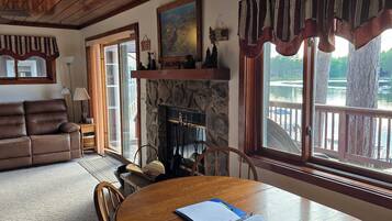 A cozy living room with a fireplace, a dining table, and a view of a lake through large windows.