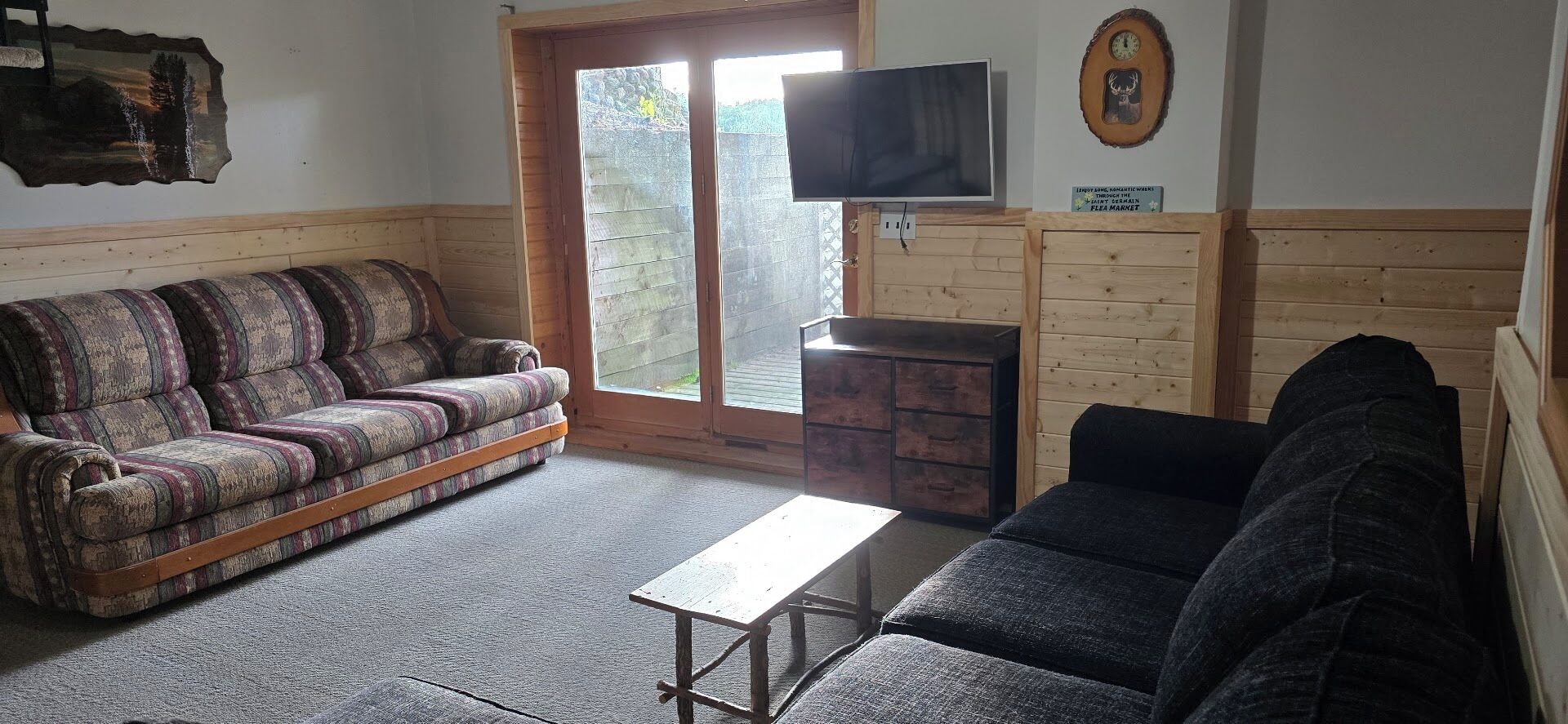 Ein Zimmer mit einer Couch, einem Tisch, einem Fernseher und einem Holzschrank.