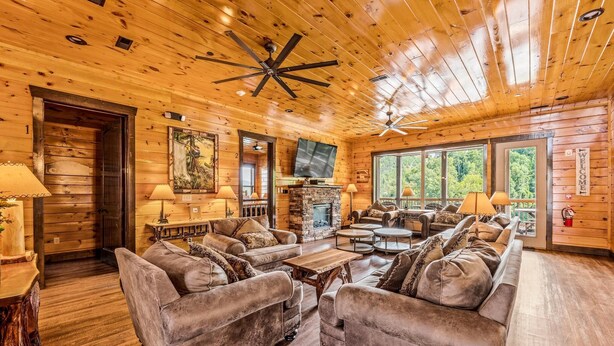 A log cabin interior with a fireplace, multiple seating areas, and large windows. - The Majestic Pine Retreat (Gatlinburg)